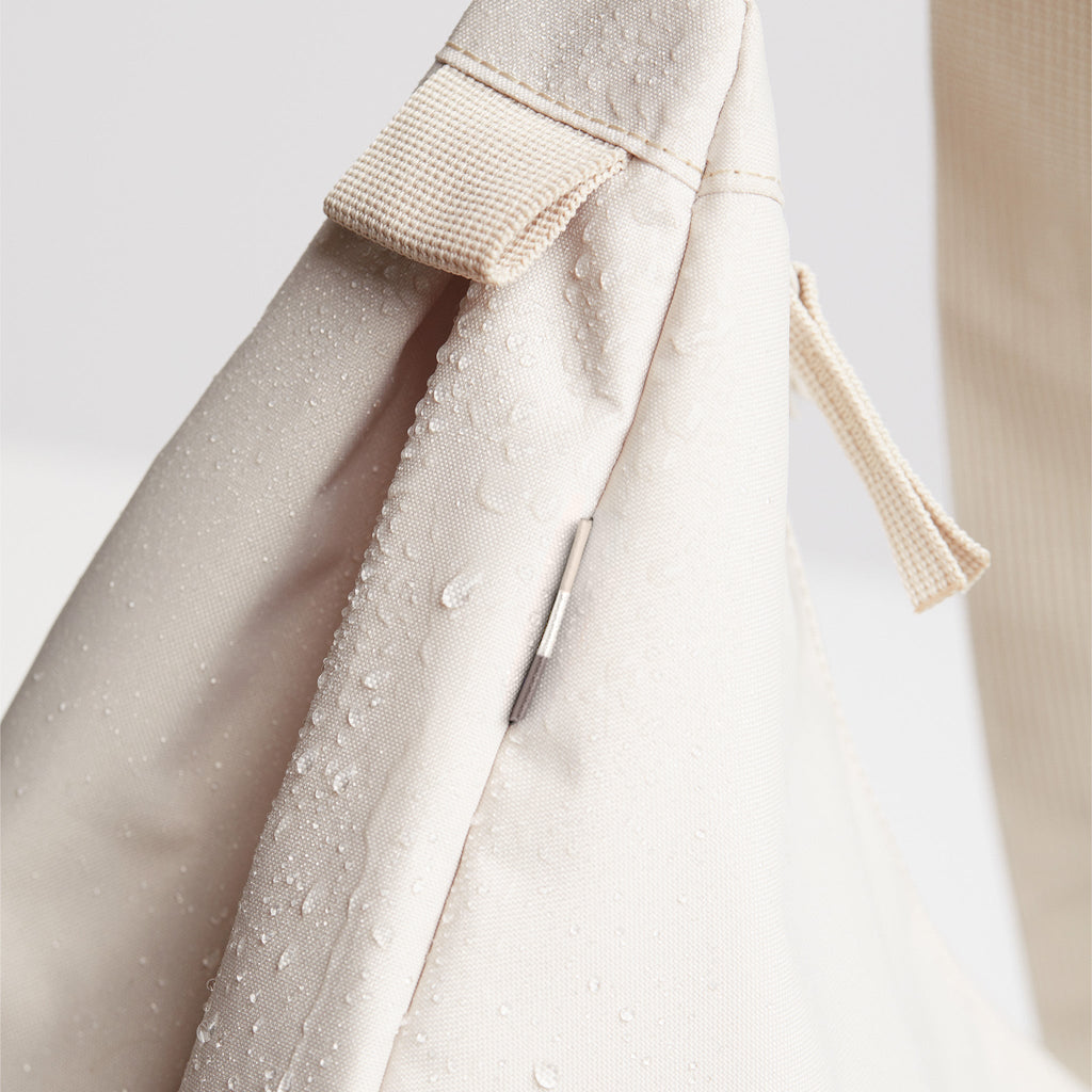 MOON BAG SMALL Tasche in soft shell (warmes Cremeweiß), Detailaufnahme mit Wassertropfen und Reißverschluss.