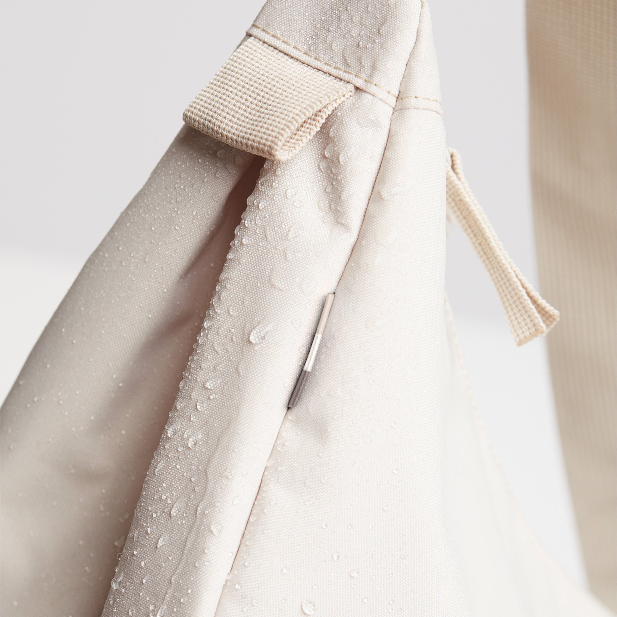 MOON BAG SMALL Tasche in soft shell (warmes Cremeweiß), Detailaufnahme mit Wassertropfen und Reißverschluss.