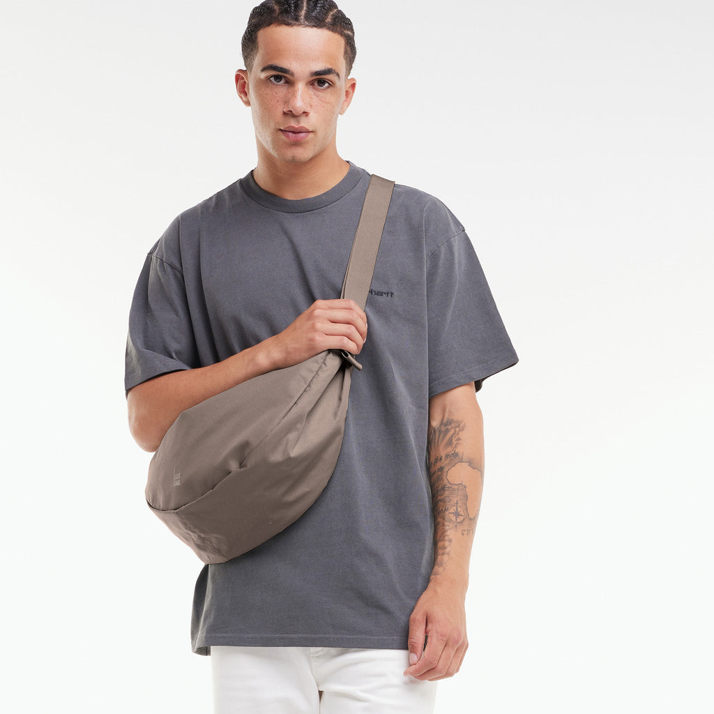 MOON BAG LARGE Tasche in oyster (klassisches Taupe-Braun) von einem Mann über der Schulter getragen.