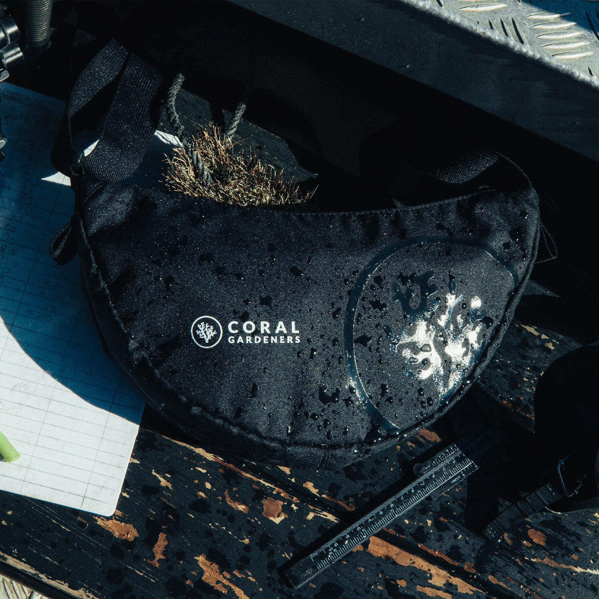 MOON BAG SMALL Tasche in black (Schwarz) mit Wassertropfen auf feuchtem Holzbrett, daneben Notizen und Messwerkzeug.