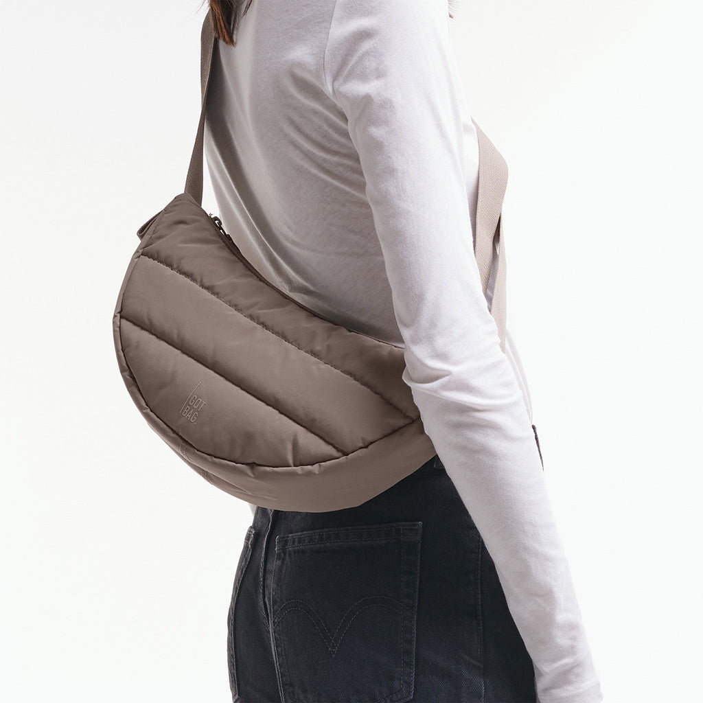 PUFFER MOON BAG SMALL Tasche in oyster (klassisches Taupe-Braun) von einer Frau crossbody getragen.