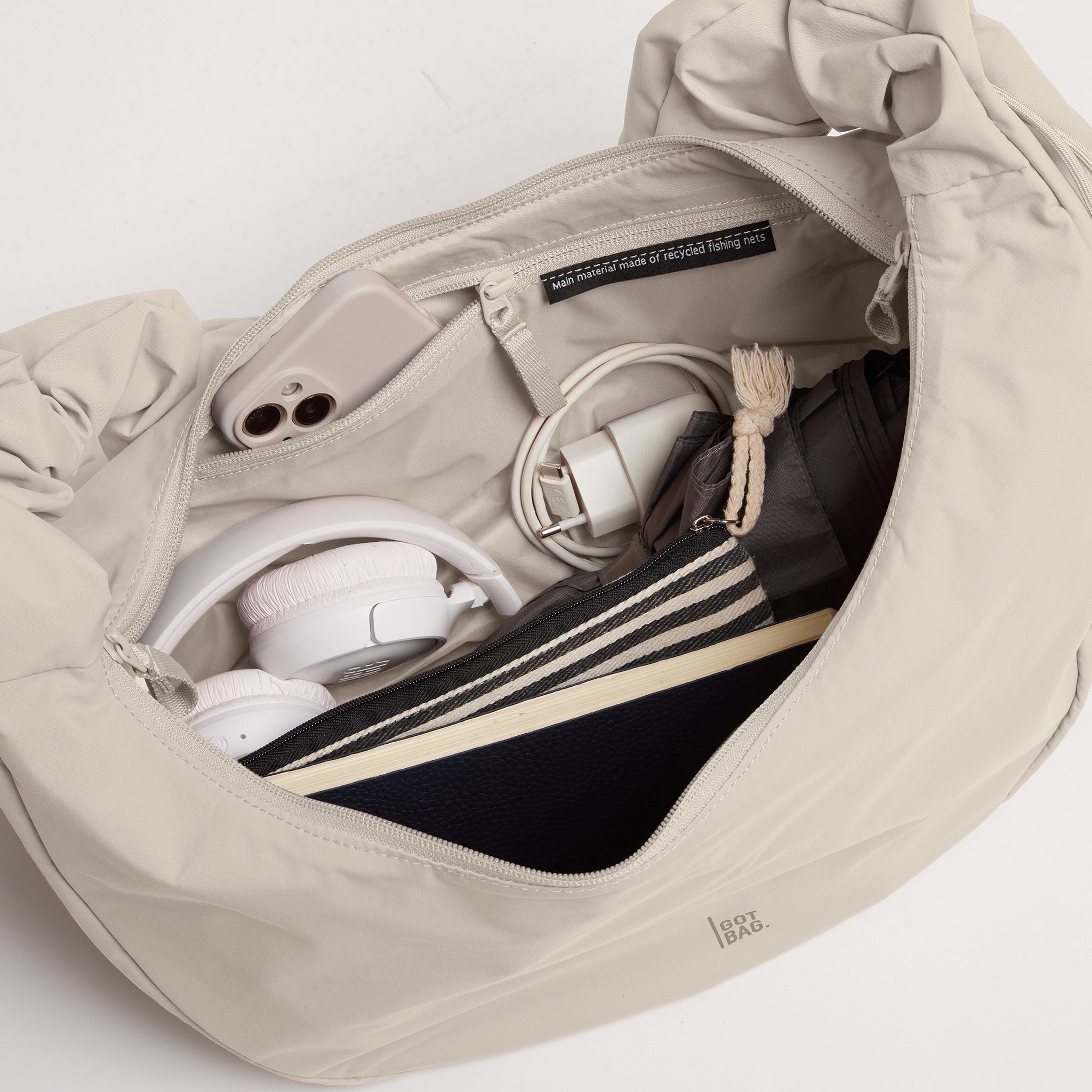 MOON BAG RUFFLE Tasche in soft shell (warmes Cremeweiß), offenes Inneres mit Smartphone, Kopfhörern und Ladegerät.