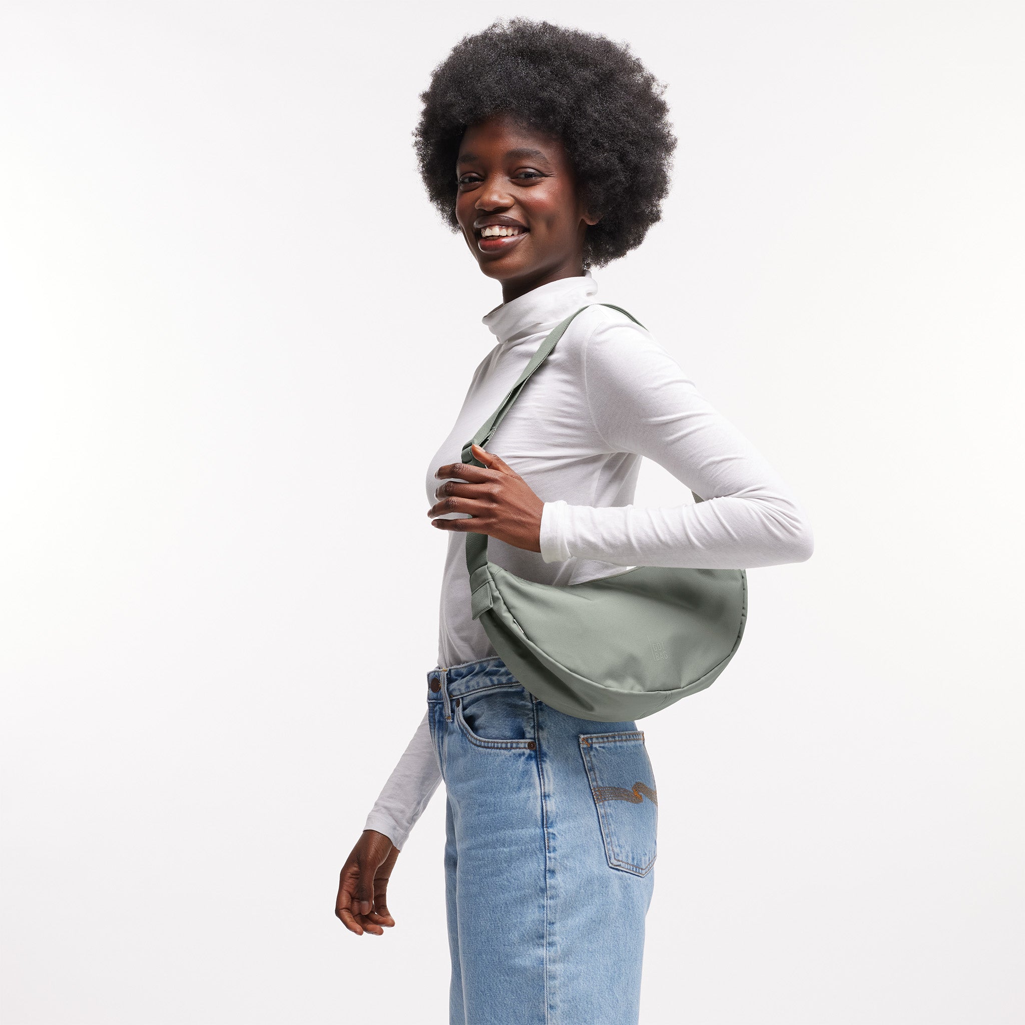 MOON BAG SMALL Tasche in bass (Salbeigrün) von einer Frau über der Schulter getragen.