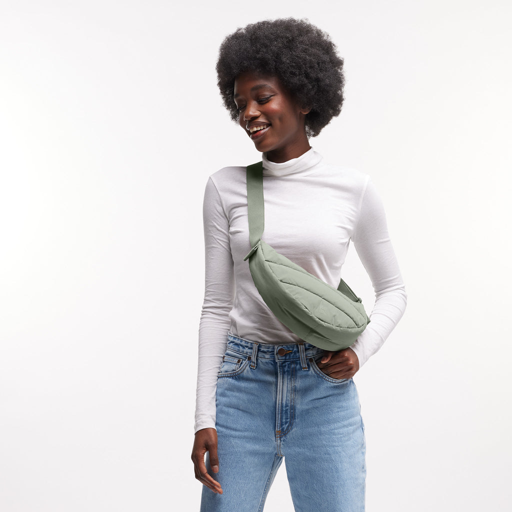 PUFFER MOON BAG SMALL Tasche in bass (Salbeigrün) von einer Frau crossbody getragen.