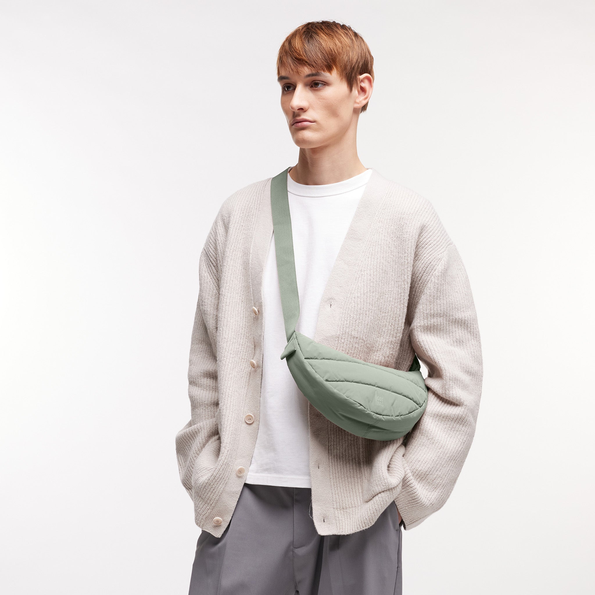 PUFFER MOON BAG SMALL Tasche in bass (Salbeigrün) von einem Mann crossbody getragen.