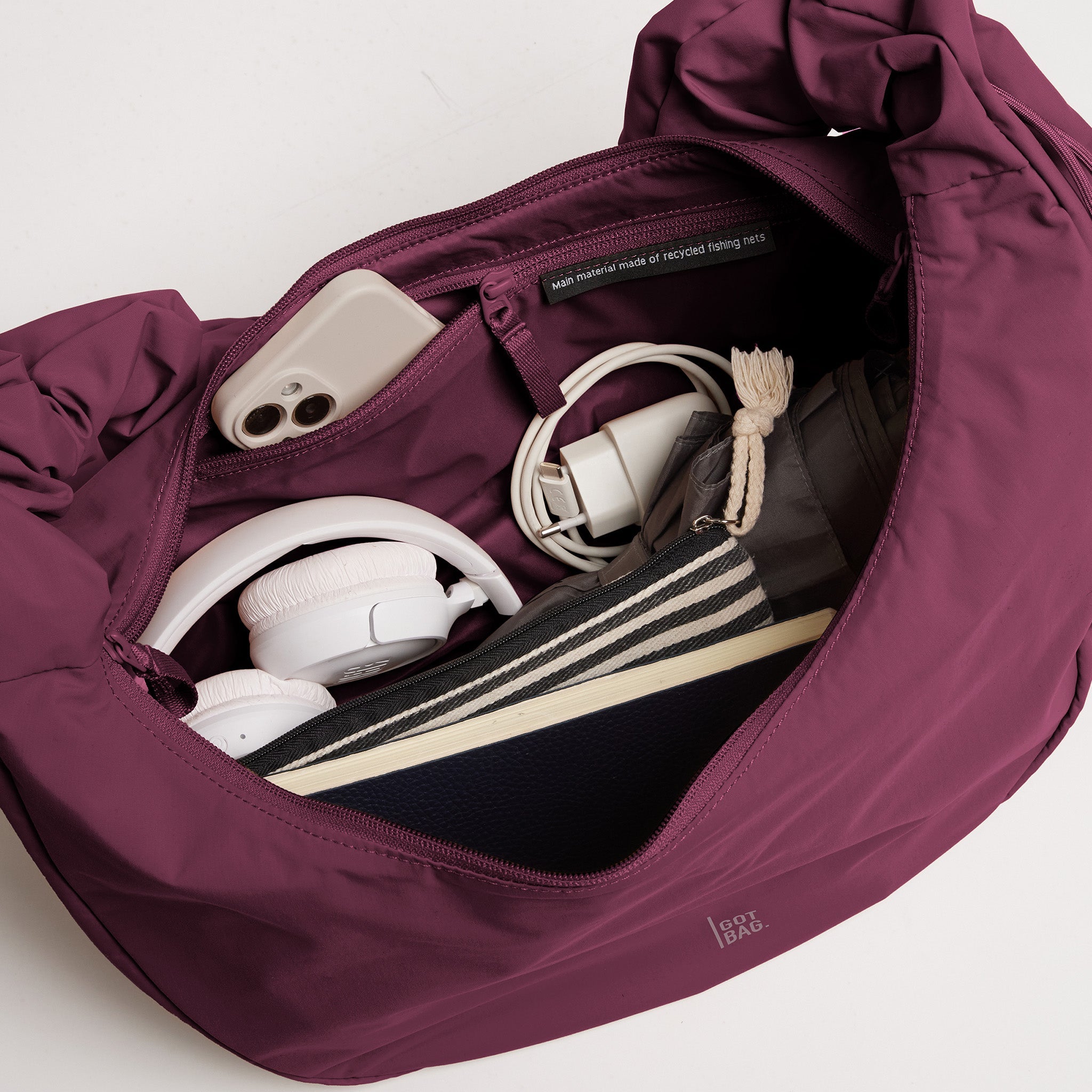 MOON BAG RUFFLE Tasche in kraken (Weinrot), Innenansicht mit Handy, Kopfhörern, Material aus recycelten Fischernetzen.