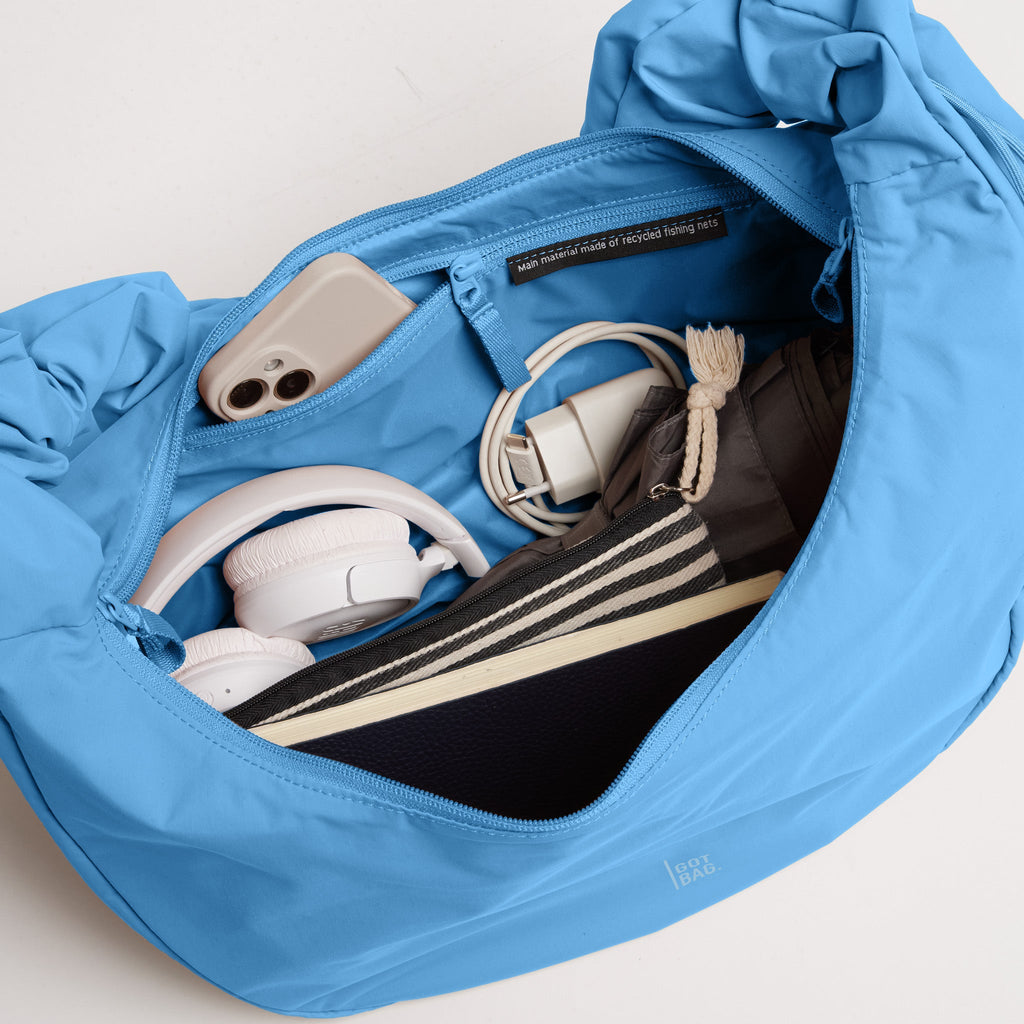 MOON BAG RUFFLE Tasche in aqua (leuchtendes Hellblau) als Detailaufnahme des geöffneten Innenbereichs mit Inhalt.