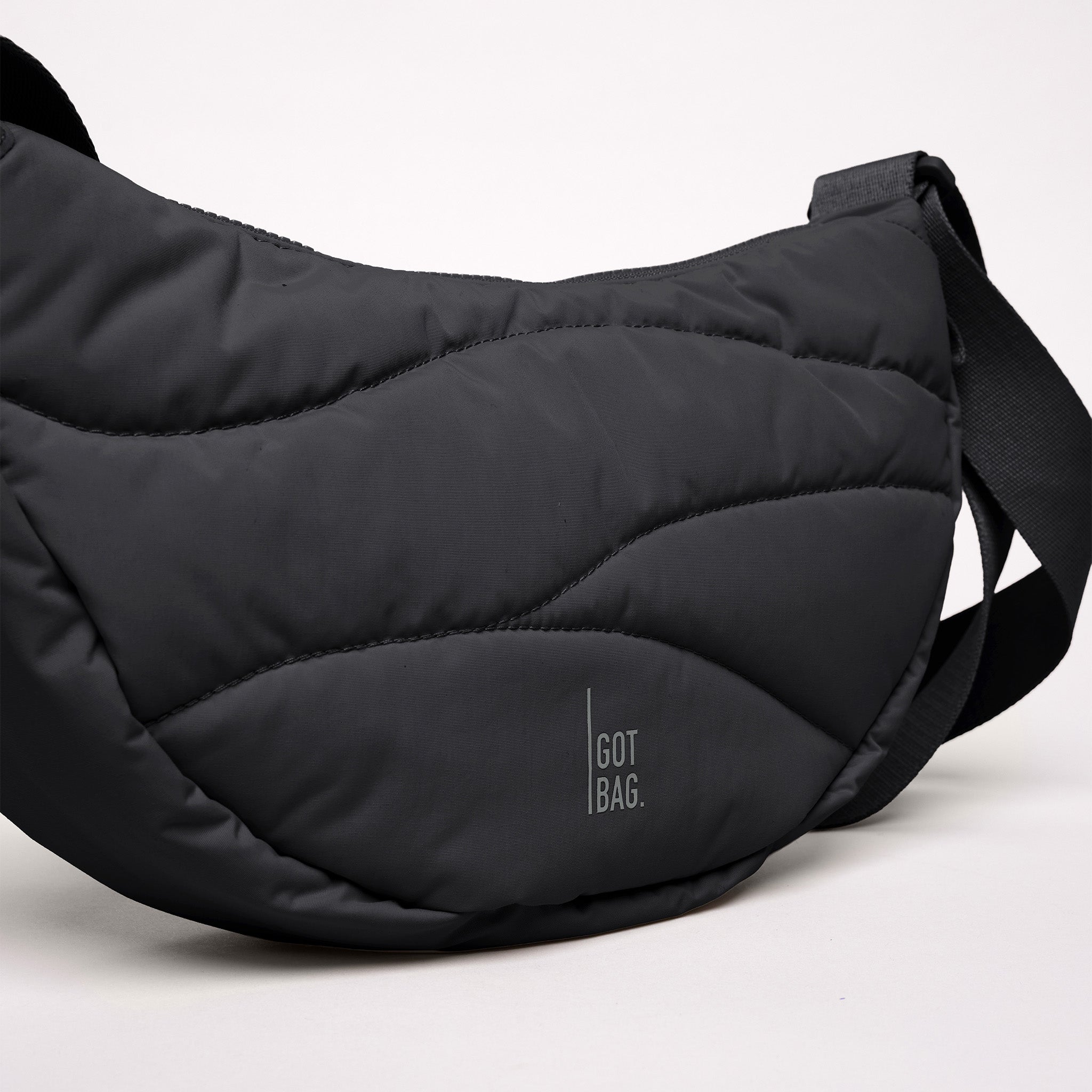 WAVY PUFFER MOON BAG Tasche in black (Schwarz) mit wellenförmiger Steppung auf weißem Hintergrund.