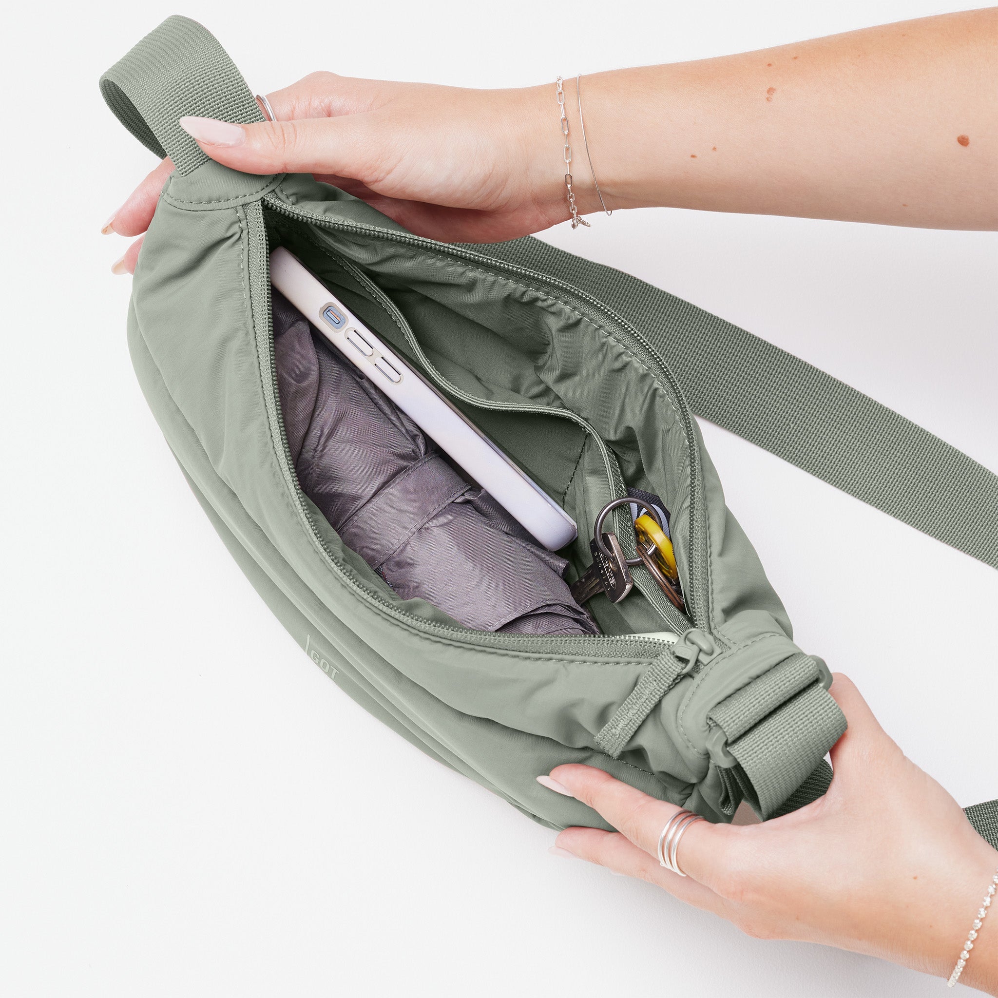 PUFFER MOON BAG SMALL Tasche in bass (Salbeigrün) von einer Frau geöffnet, die den Inhalt zeigt (Handy, Regenschirm, Schlüssel).