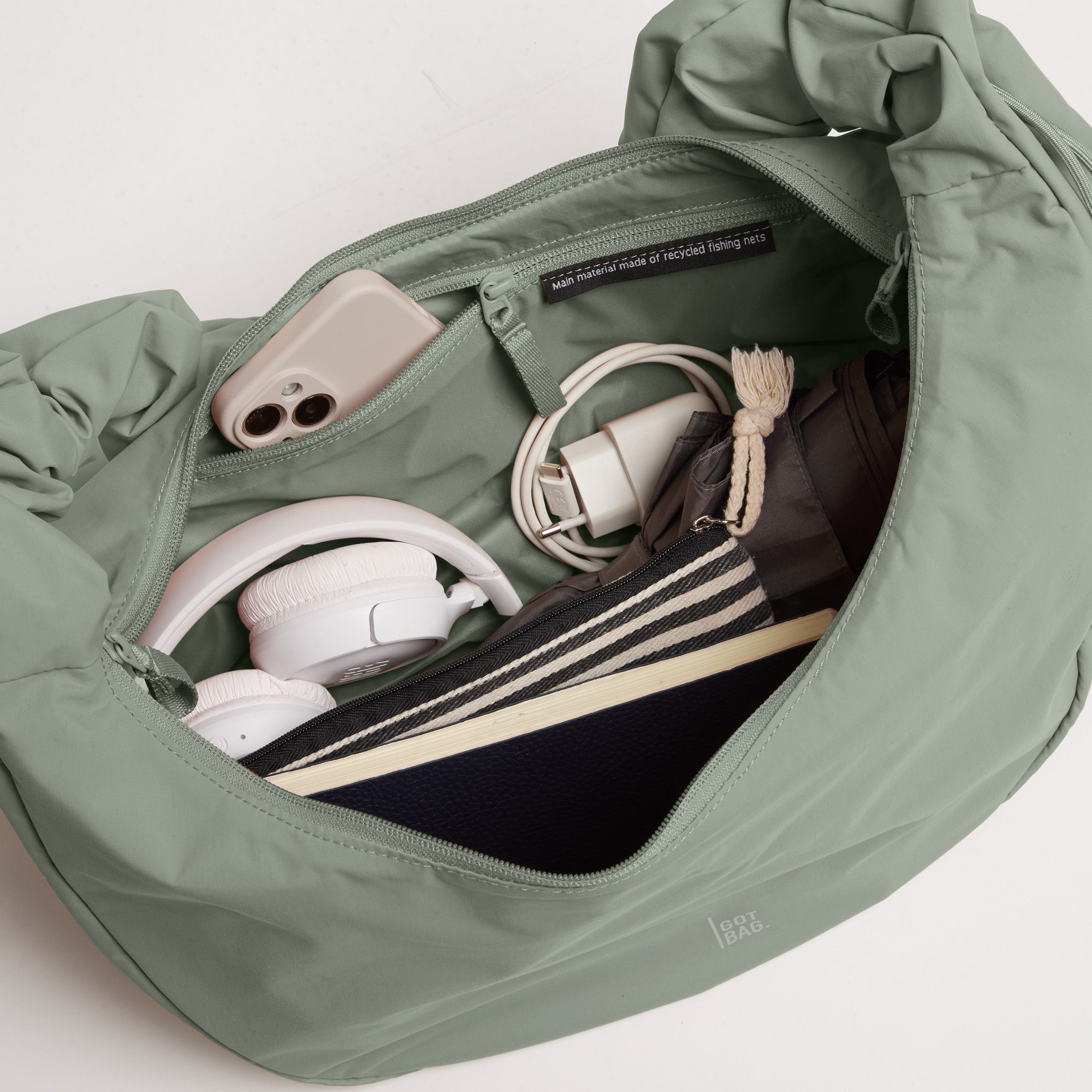 MOON BAG RUFFLE Tasche in bass (Salbeigrün) Innenansicht mit Handy, Kopfhörern und Ladekabel.