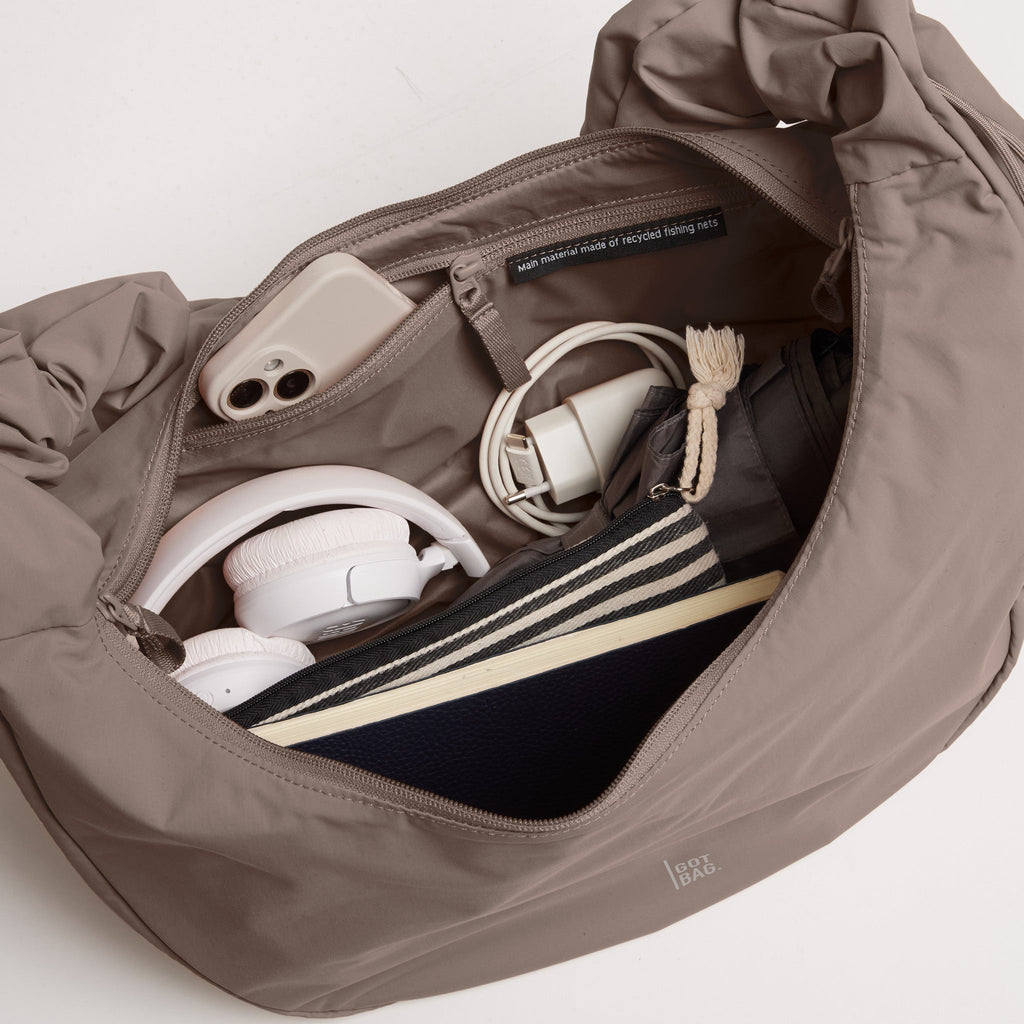 MOON BAG RUFFLE Tasche in oyster (klassisches Taupe-Braun) Innenansicht mit Smartphone, Kopfhörern, Ladegerät und gestreifter Tasche.