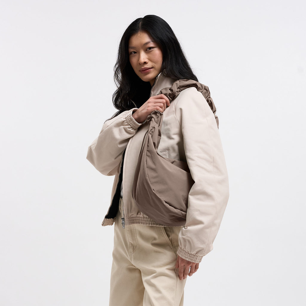 MOON BAG RUFFLE Tasche in oyster (klassisches Taupe-Braun) von einer Frau über der Schulter getragen.