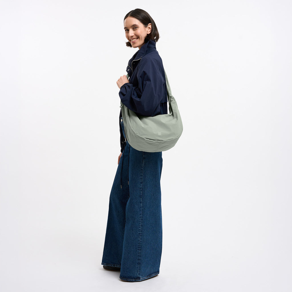 MOON BAG RUFFLE Tasche in bass (Salbeigrün) von einer Frau crossbody getragen.
