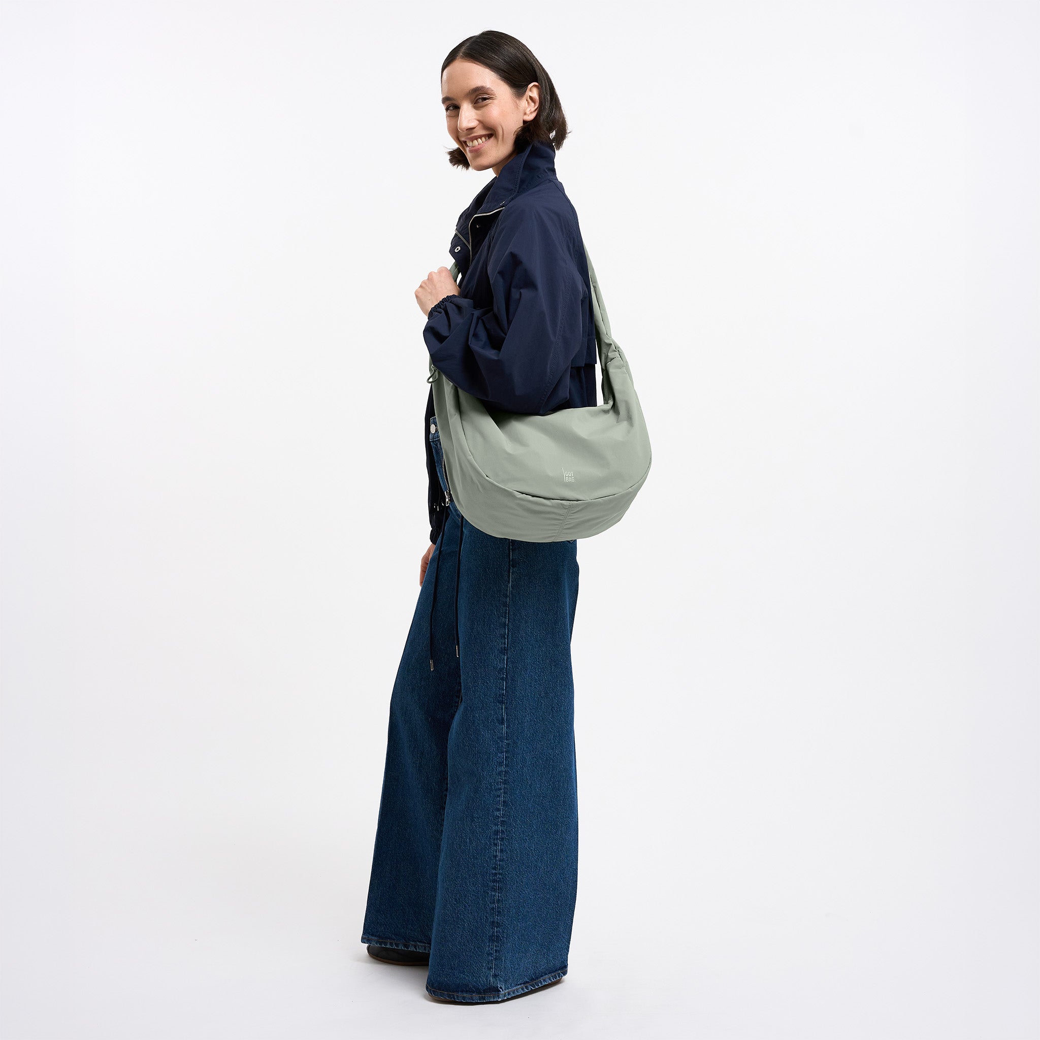 MOON BAG RUFFLE Tasche in bass (Salbeigrün) von einer Frau crossbody getragen.