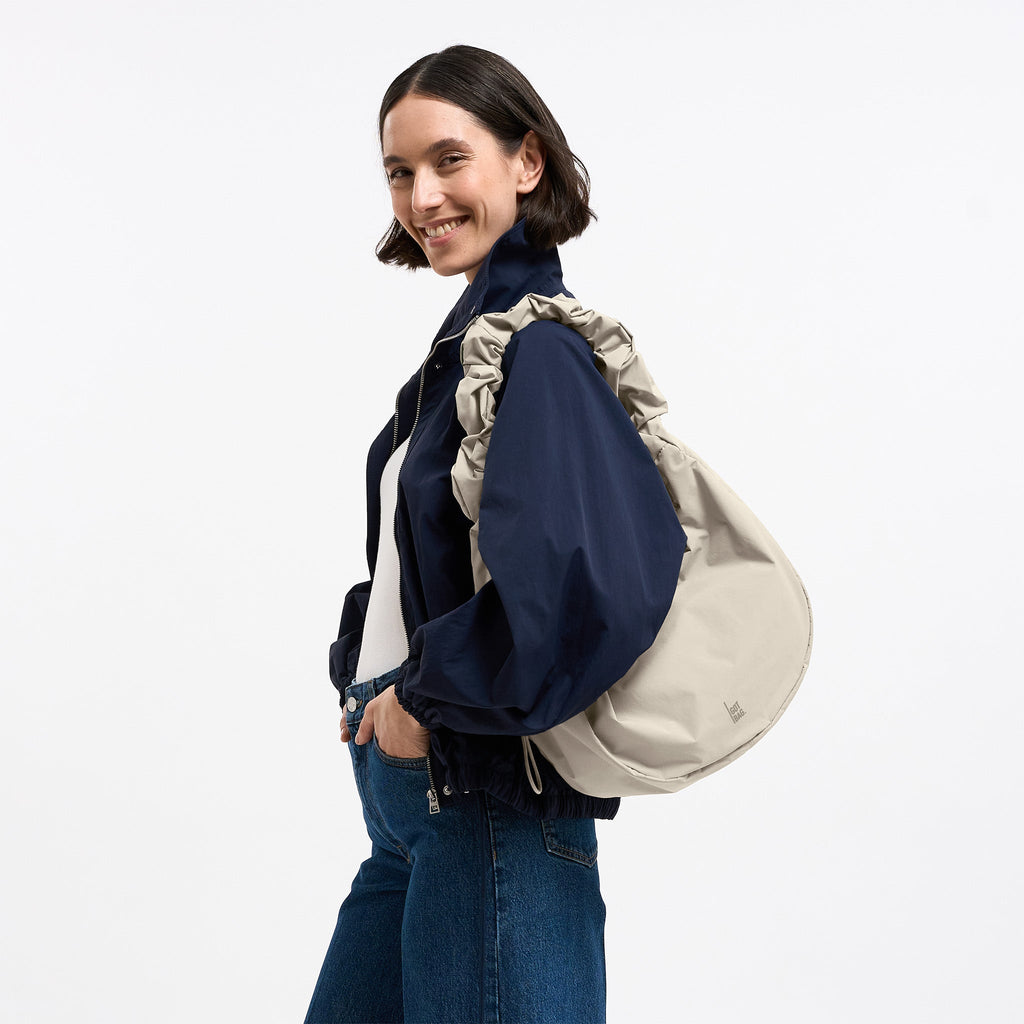 MOON BAG RUFFLE Tasche in soft-shell (warmes Cremeweiß) von einer Frau über der Schulter getragen.