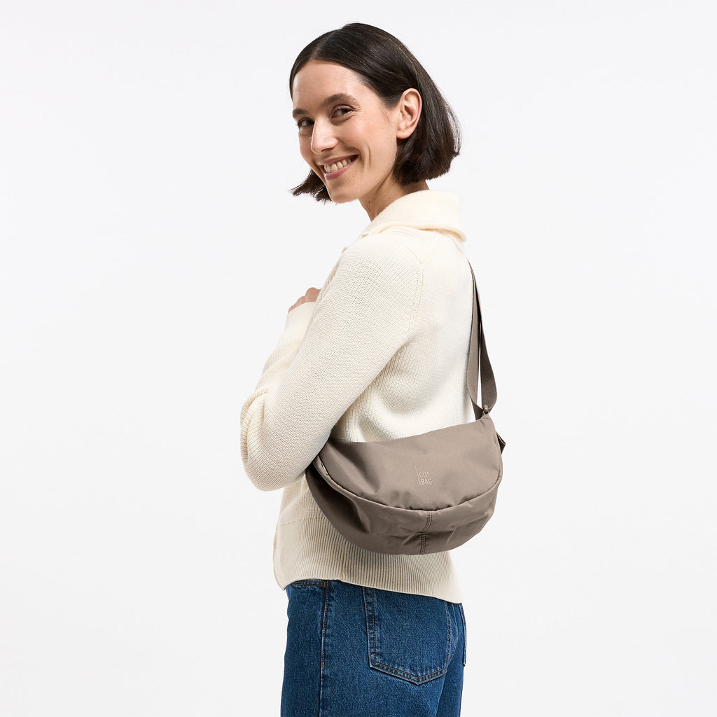 MOON BAG SMALL MONOCHROME Tasche in seal (dunkler Beigeton) von einer Frau crossbody getragen.