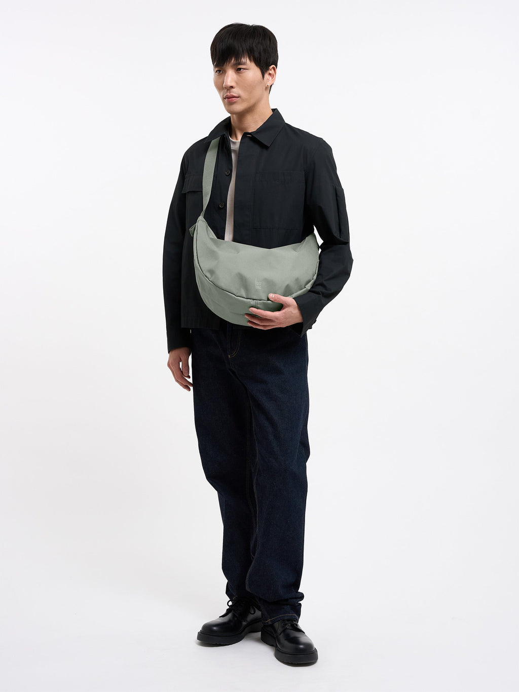 MOON BAG LARGE Tasche in bass (Salbeigrün) von einem Mann crossbody getragen.